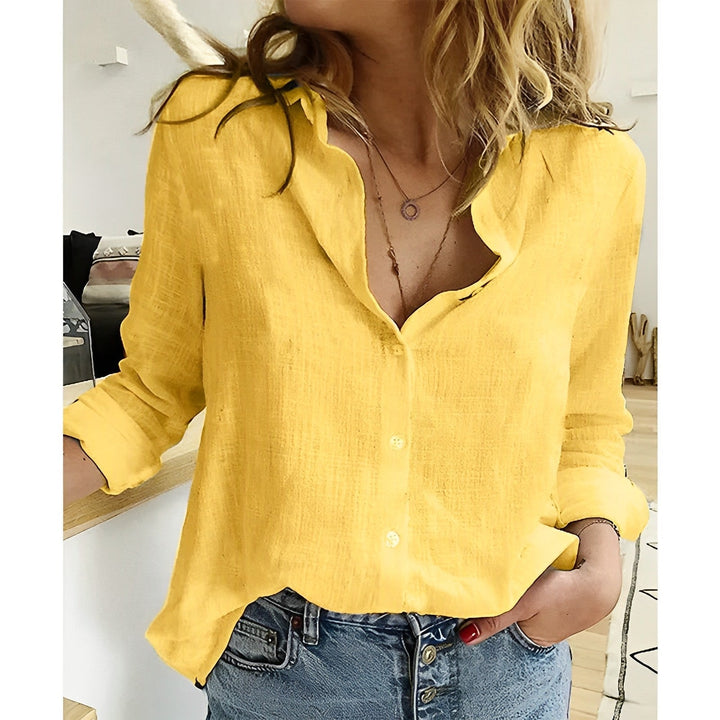 Bright yellow linen-look button-up blouse with long sleeves and a relaxed, loose fit paired with blue denim jeans.