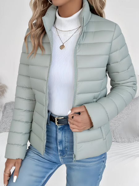 Sage green lightweight quilted puffer jacket with a high stand collar and full-length zip, worn over a white turtleneck.