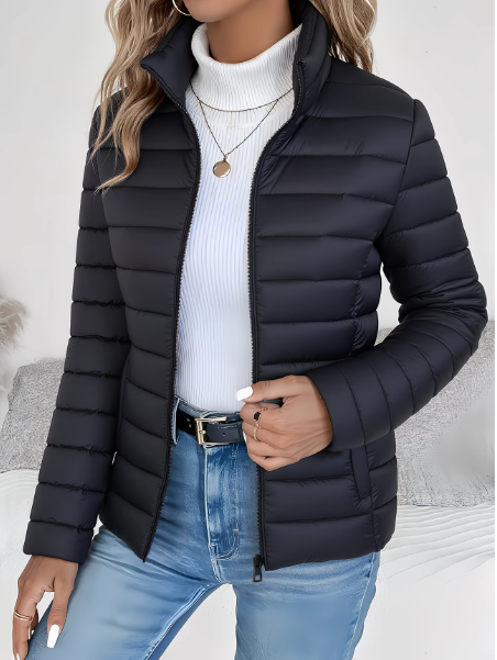 Black quilted puffer jacket with a high stand collar, full-length zip, and tailored fit worn over a white turtleneck.