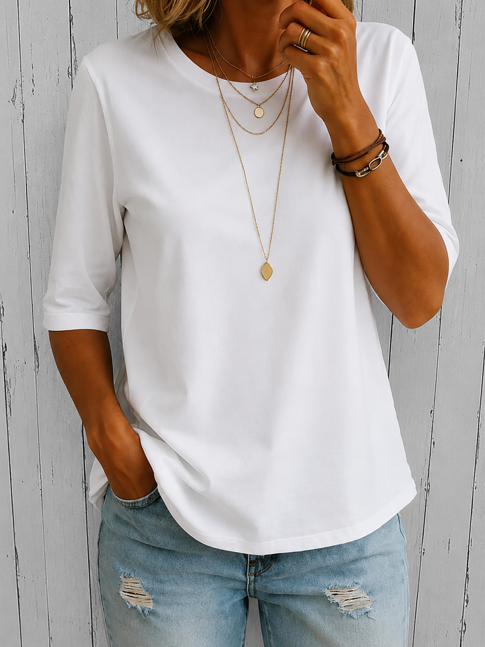 Woman wearing a white, relaxed-fit round neck top with half sleeves and a curved hem, styled with light wash distressed jeans.
