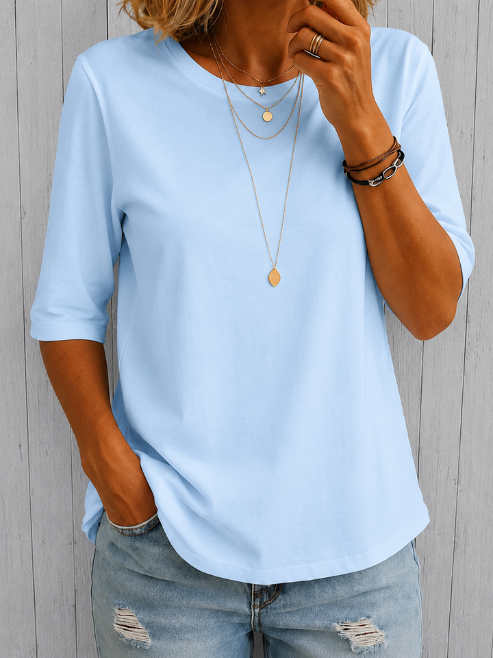 Light blue round-neck top with half sleeves and a relaxed fit, styled with jeans and layered gold necklaces.
