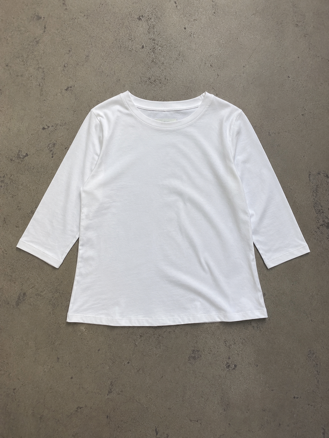 White round-neck top with half sleeves and a relaxed fit, laid flat on a neutral textured surface.
