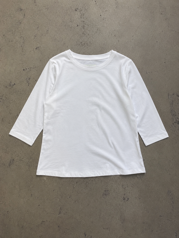 White round-neck top with half sleeves and a relaxed fit, laid flat on a neutral textured surface.