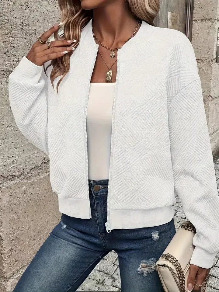 White textured zip-up cardigan with a ribbed stand collar, cuffs, and hem, styled over a white top and distressed blue jeans.