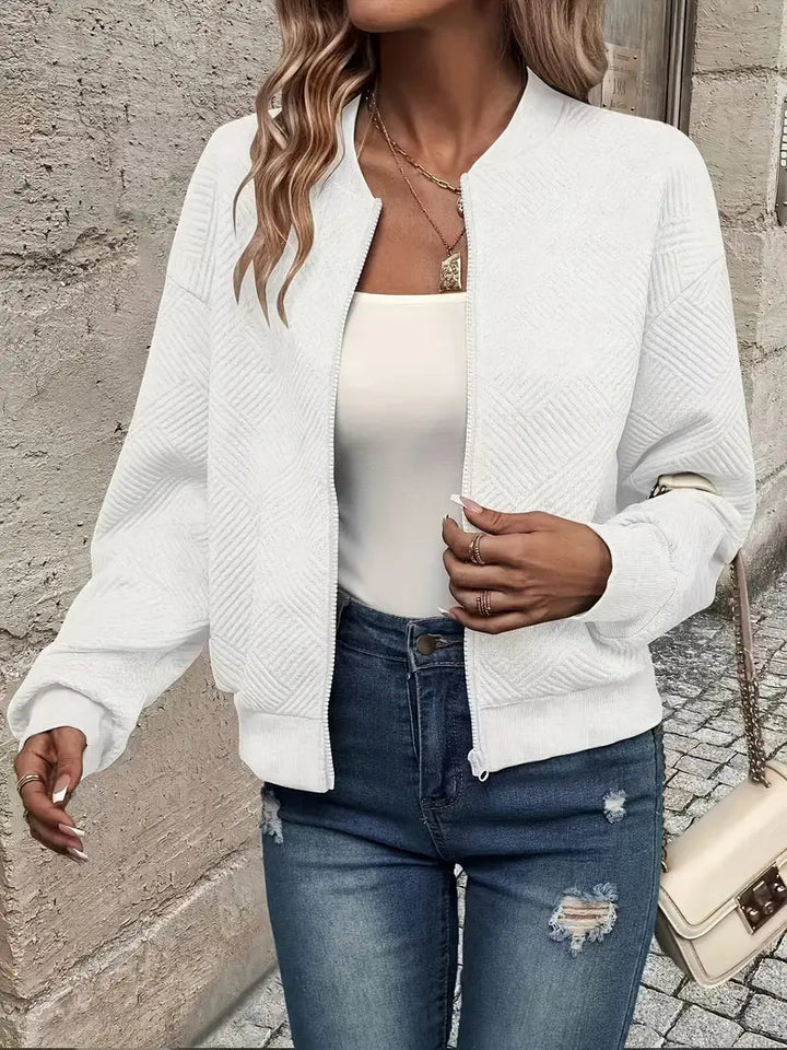 White textured zip-up cardigan with a ribbed stand collar, cuffs, and hem, worn over a white top and distressed blue jeans.