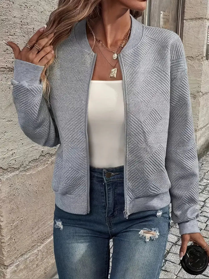 Grey textured zip-up cardigan with a ribbed stand collar, cuffs, and hem worn over a white top and blue jeans.