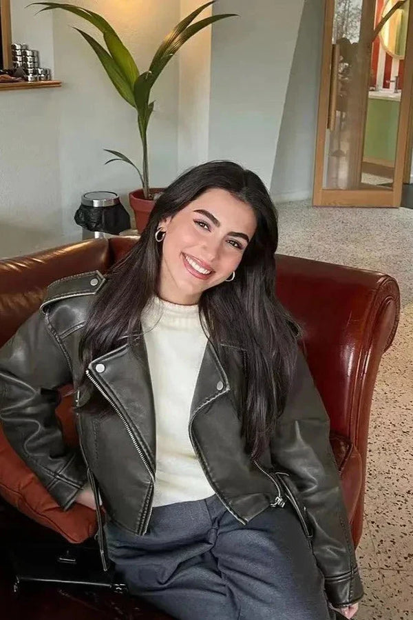 Woman wearing a black cropped faux leather biker jacket with an asymmetric zip and buckled waist belt.
