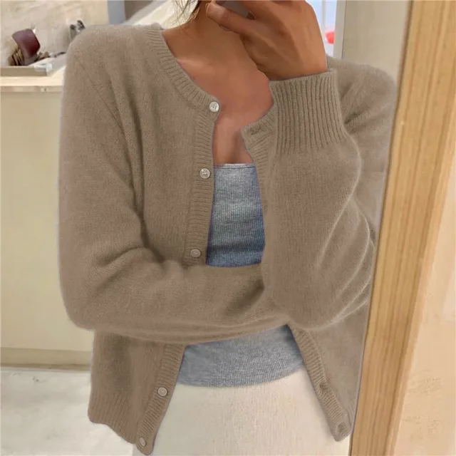 Beige knit crew neck cardigan with long sleeves, ribbed cuffs, and a button-through front worn over a grey top.