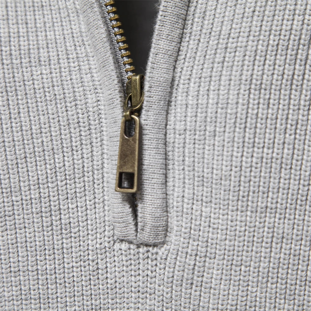 Close-up of a light grey men's quarter-zip knit sweater featuring a metallic bronze zipper pull and ribbed texture.
