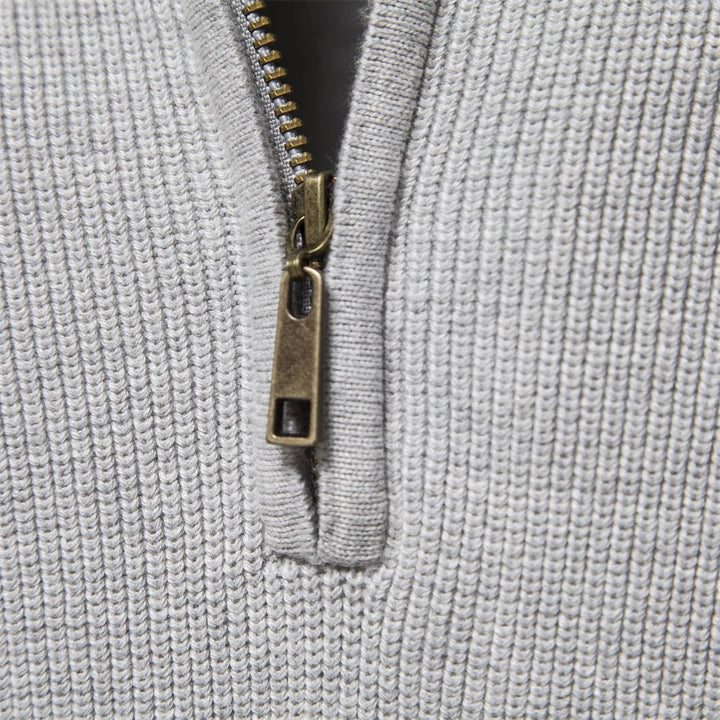 Close-up of a light grey men's quarter-zip knit sweater featuring a metallic bronze zipper pull and ribbed texture.