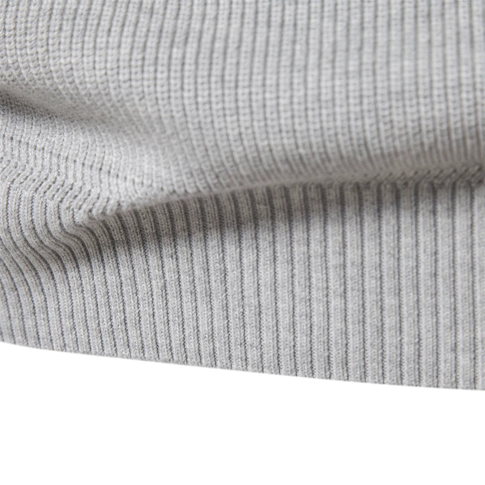 Close-up of a light grey men's quarter-zip sweater featuring a soft, midweight ribbed knit texture and hem.