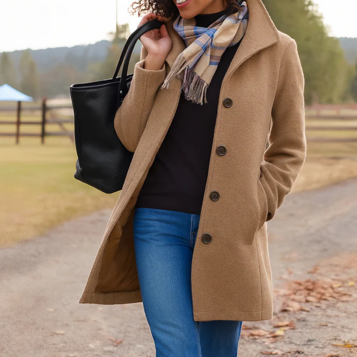 Camel-colored mid-length wool coat with a button-up front, collared neckline, and side pockets worn over jeans.