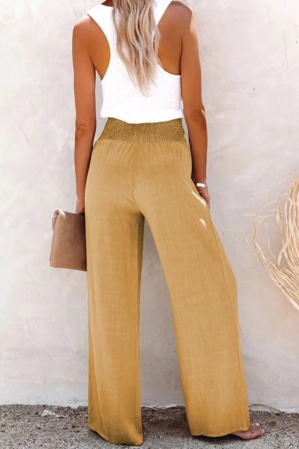 Woman wearing tan high-waisted wide-leg linen trousers with a smocked waistband and a white tank top.