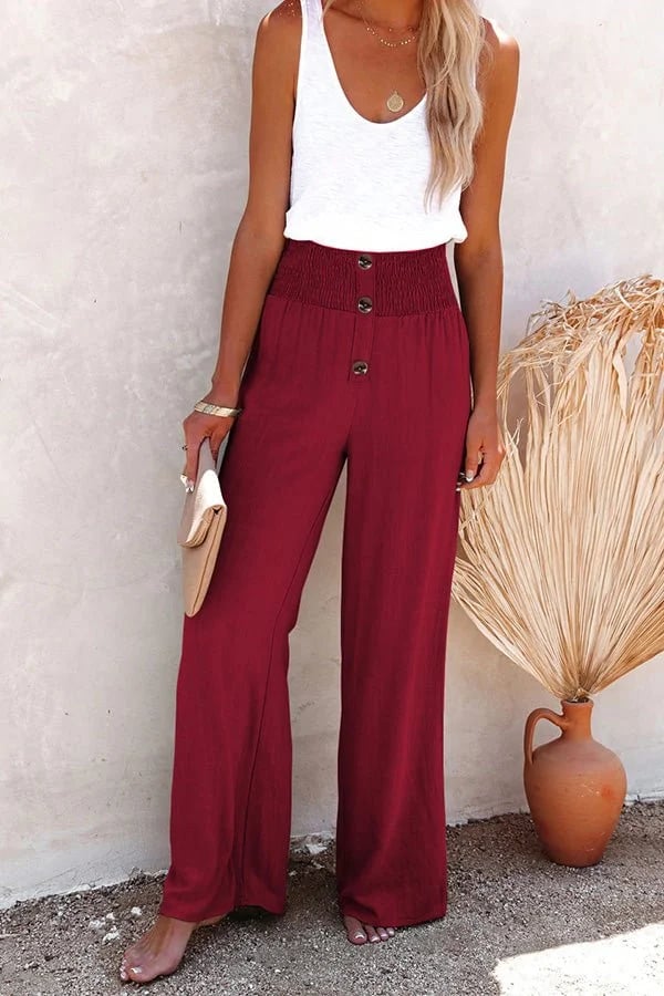 Burgundy high-waisted wide-leg linen trousers featuring a smocked waistband and decorative front buttons.