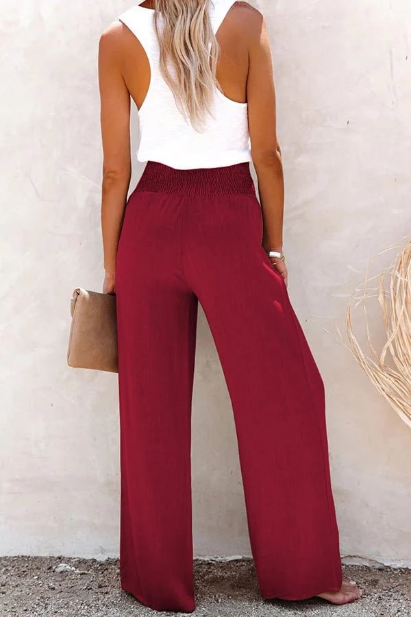 Burgundy high-waisted wide-leg linen trousers with a smocked waistband, worn with a white tank top.