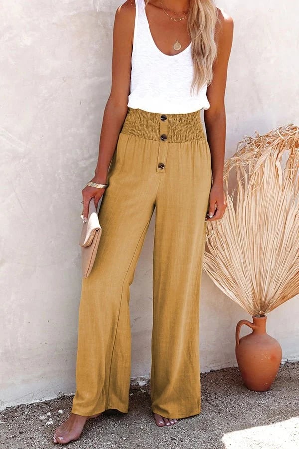 Mustard yellow high-waisted wide-leg linen trousers with a smocked waistband and decorative front buttons.