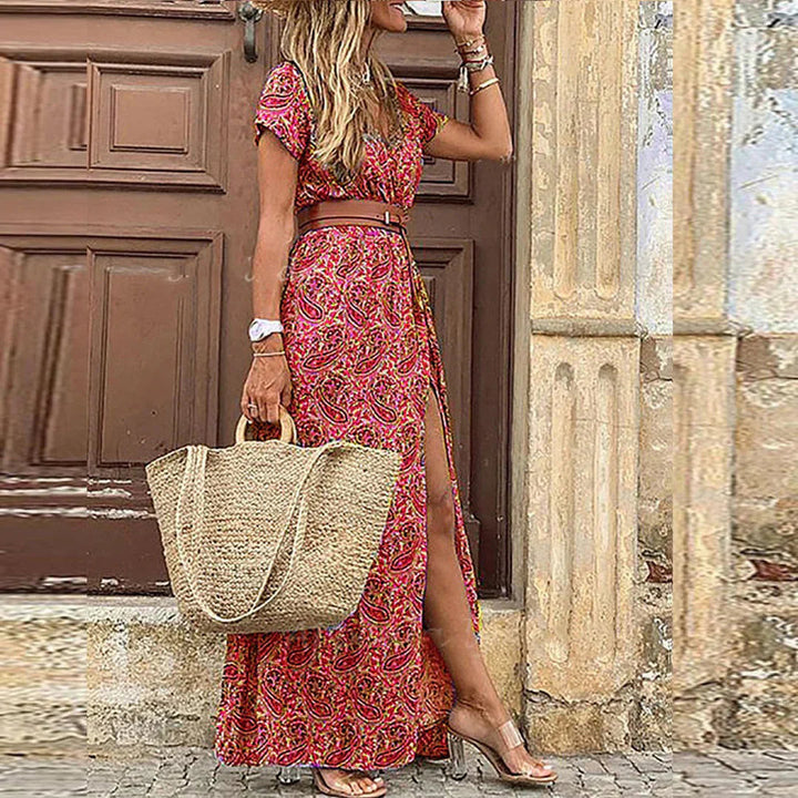 Boho floral maxi dress with V-neck, flutter sleeves, and side slit, styled with a brown belt and straw tote bag.
