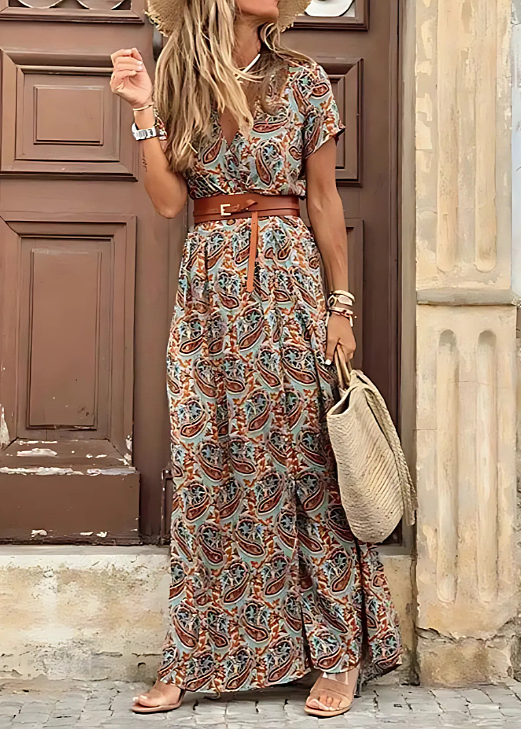 Woman wearing a boho floral maxi dress with a V-neck, flutter sleeves, side slit, and a brown leather waist belt.