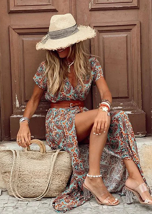 Woman wearing a boho floral maxi dress with a V-neck, flutter sleeves, and high side slit, styled with a straw hat and bag.