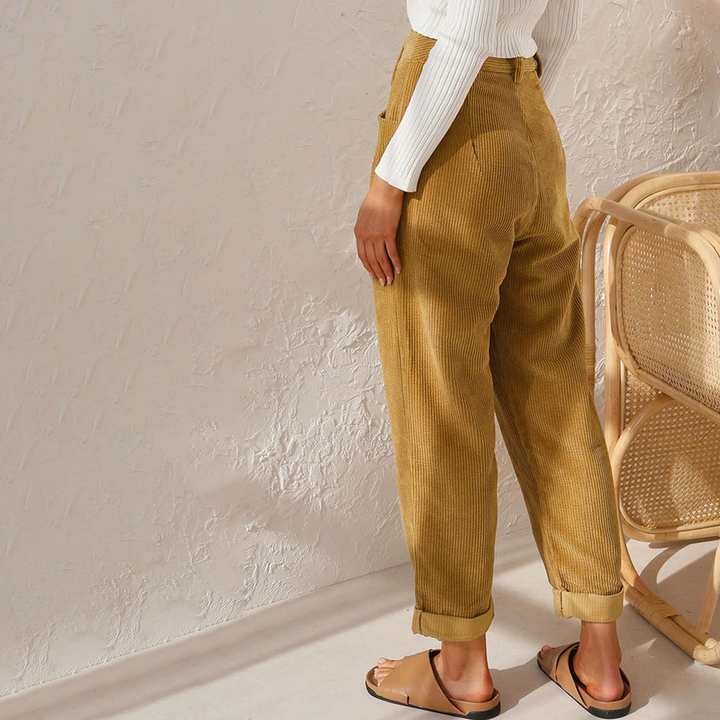 Mustard yellow high-waisted corduroy trousers with a relaxed fit and turn-up hems, paired with a white top and sandals.