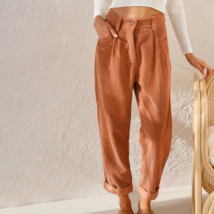 High-waisted rust-colored corduroy trousers with a relaxed leg, button-front closure, and folded turn-up hems.