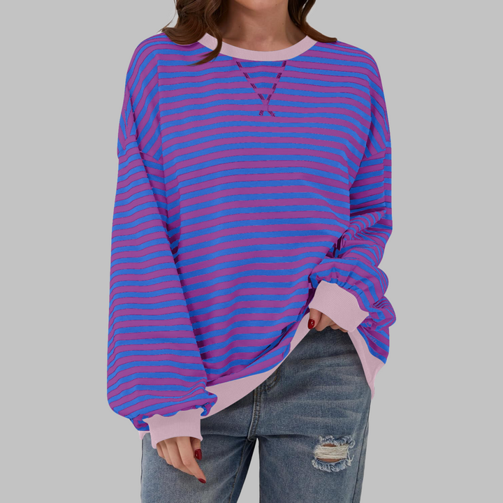 Oversized blue and purple striped sweatshirt with a pink ribbed crew neckline and cuffs, worn with distressed jeans.