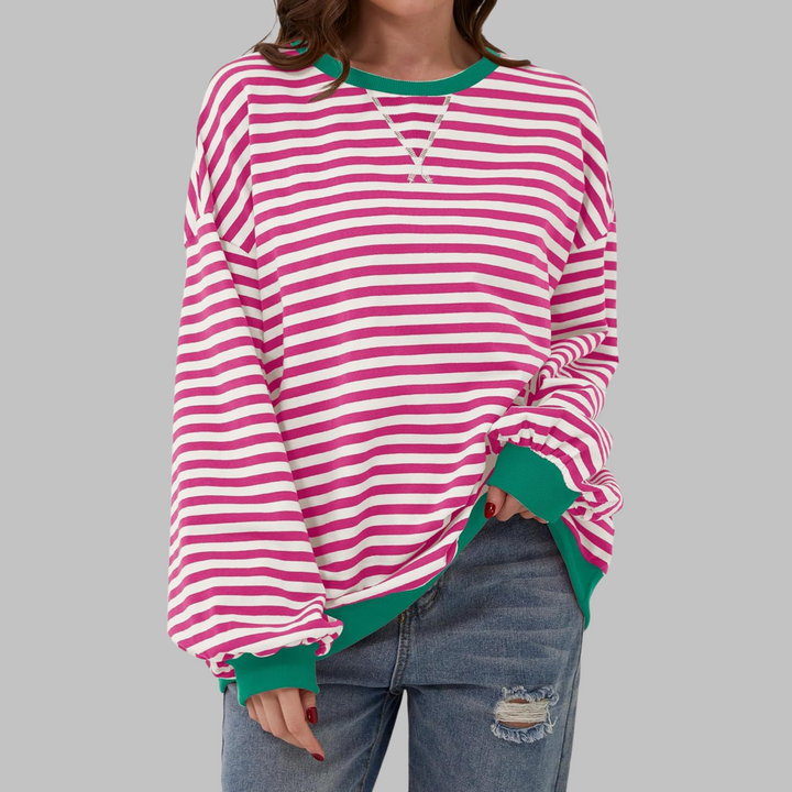 Oversized pink and white striped sweatshirt with green ribbed trim, round neckline, and relaxed fit worn with jeans.