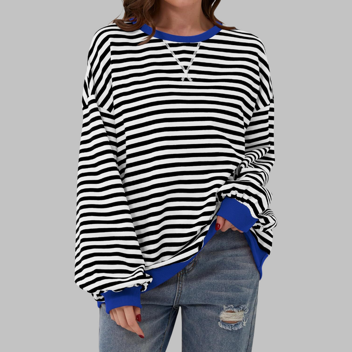 Oversized black and white striped sweatshirt with a blue ribbed crew neckline, cuffs, and hem, styled with distressed jeans.
