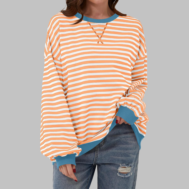 Oversized orange and white striped sweatshirt with blue ribbed trim and a round neckline, worn with distressed jeans.