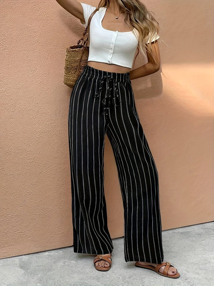 Black and white vertical pinstripe wide-leg trousers with a high-waisted drawstring, styled with a white crop top and sandals.