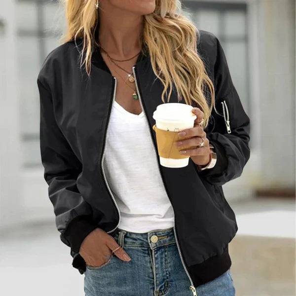 Woman wearing a black zip-up bomber jacket with elastic cuffs and a utility sleeve pocket over a white shirt and jeans.