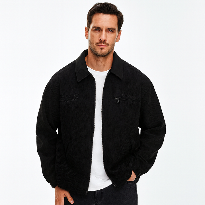 Man wearing a black corduroy zip-up jacket with a collared neckline and chest pocket over a white t-shirt.