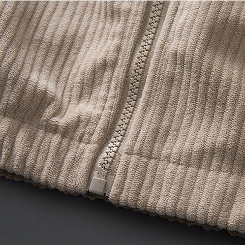 Close-up of a beige corduroy zip-up jacket featuring soft ribbed texture and a matching full-length front zipper.