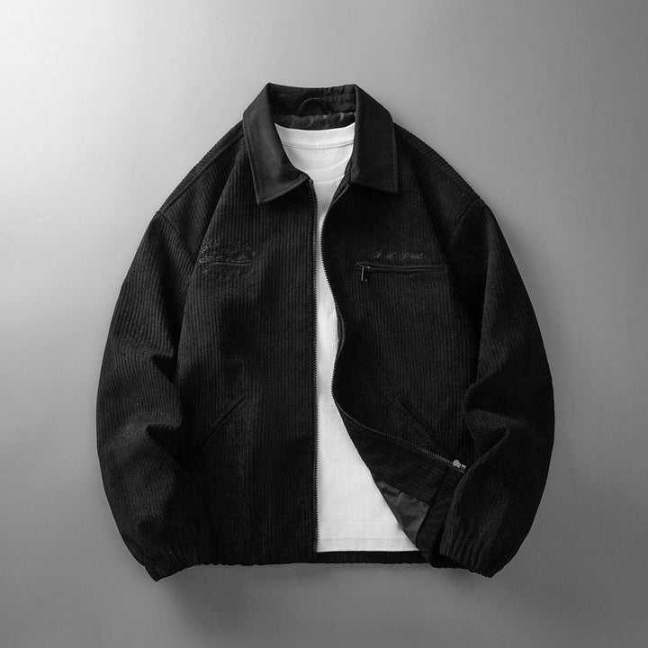 Black corduroy zip-up jacket with a collared neckline, chest pocket, and elasticated hem over a white t-shirt.