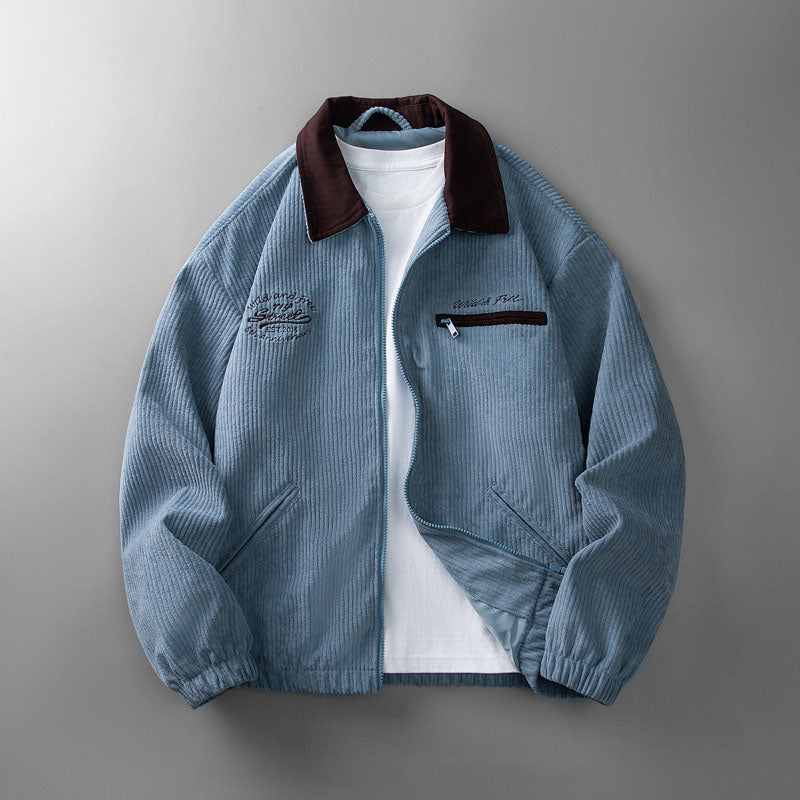 Blue corduroy zip-up jacket with a dark brown collar, embroidered chest detailing, and side pockets over a white tee.