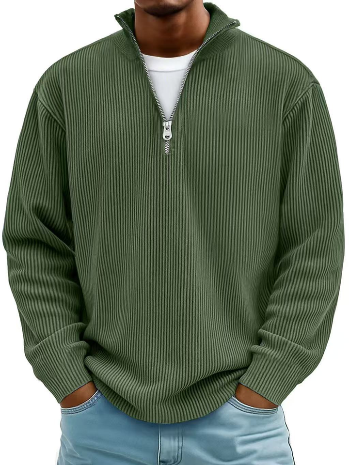 Olive green men's ribbed half-zip sweater with a stand collar, worn over a white t-shirt and light blue jeans.