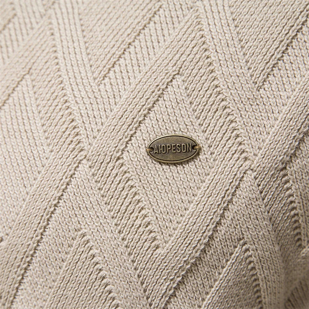 Close-up of a beige diamond-knit jumper featuring a textured pattern and a small metallic brand logo tag.