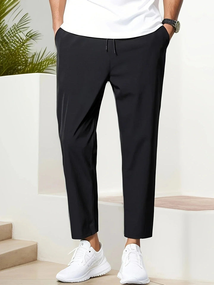 Men wearing black tapered trousers with a drawstring waist, side pockets, and a cropped ankle length.