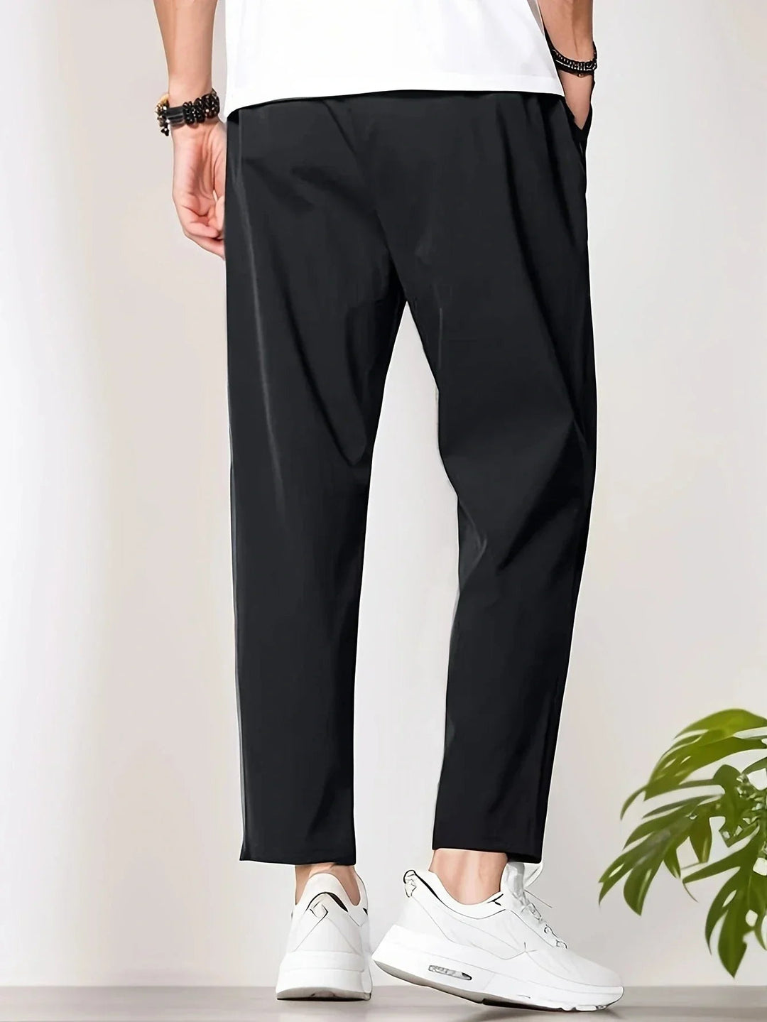 Men wearing black tapered trousers with a drawstring waist and cropped ankle length paired with white sneakers.
