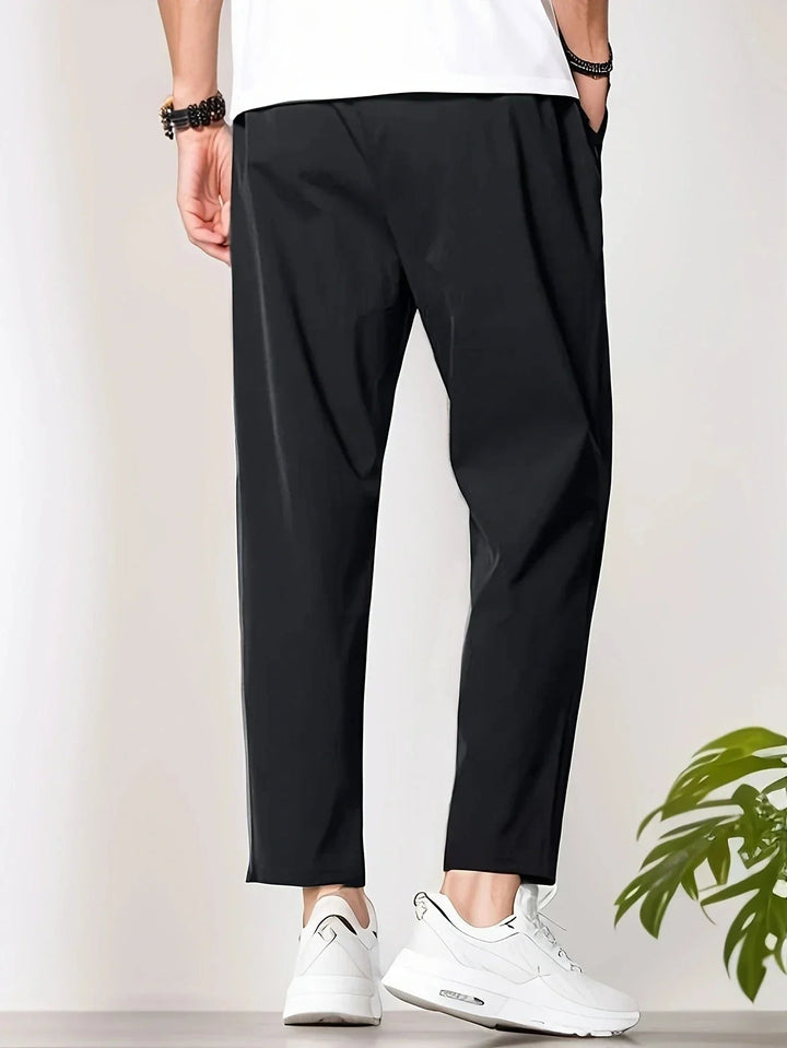 Men wearing black tapered trousers with a drawstring waist and cropped ankle length paired with white sneakers.