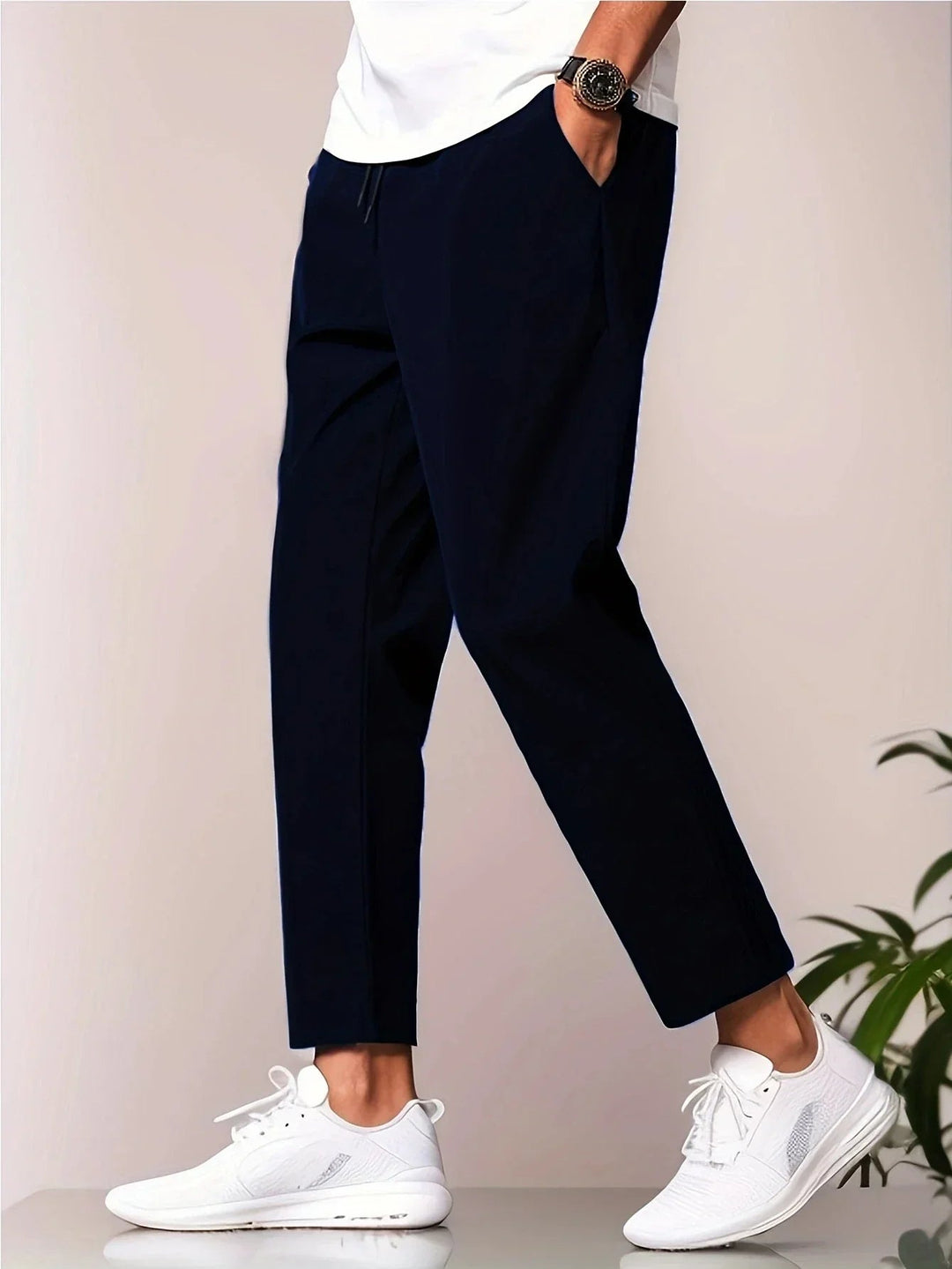Navy blue tapered trousers with a drawstring waist, side pockets, and a cropped ankle length on a model.