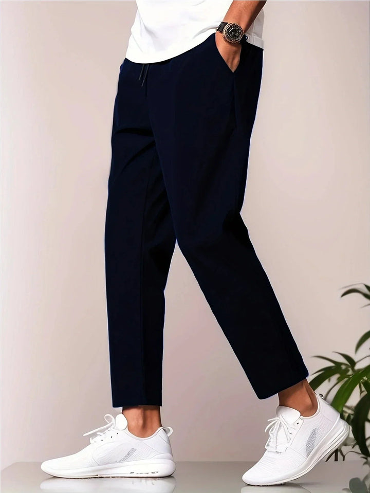 Navy blue tapered trousers with a drawstring waist, side pockets, and a cropped ankle length on a model.