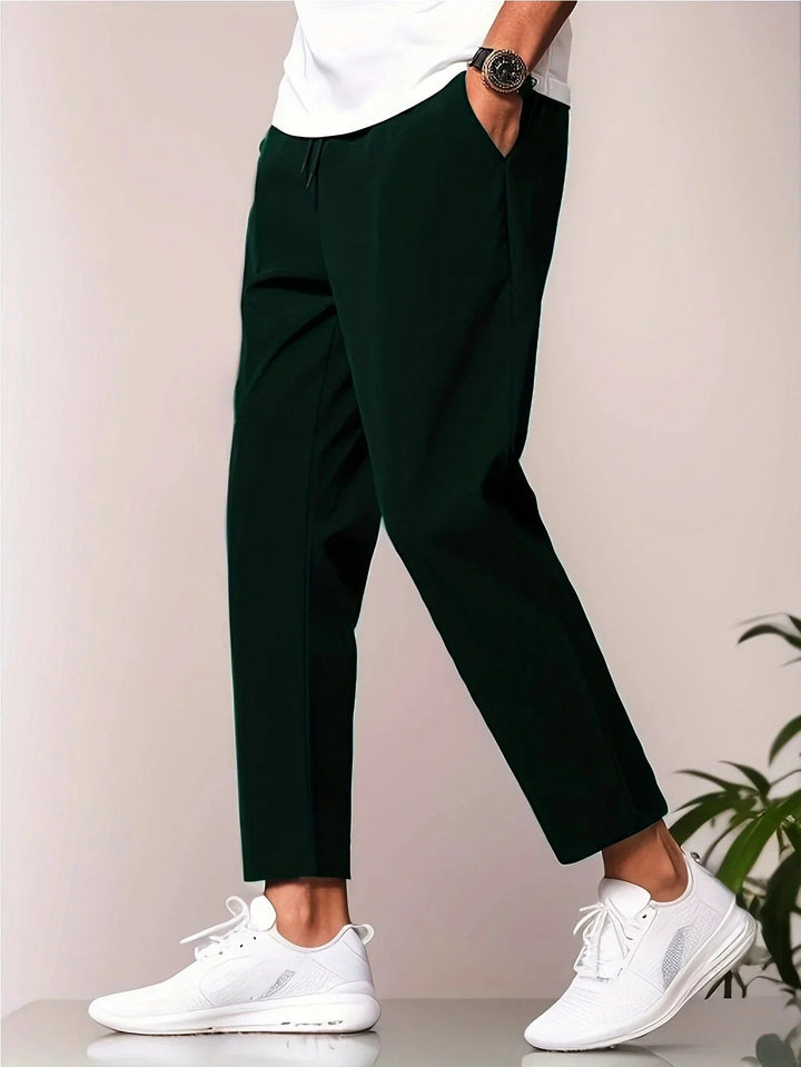 Dark green men's tapered trousers with a drawstring waist, side pockets, and a modern cropped ankle length.