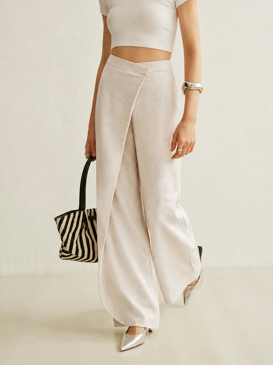 Beige high-waisted wide-leg trousers featuring a contemporary asymmetric wrap front panel and a smooth, tailored finish.