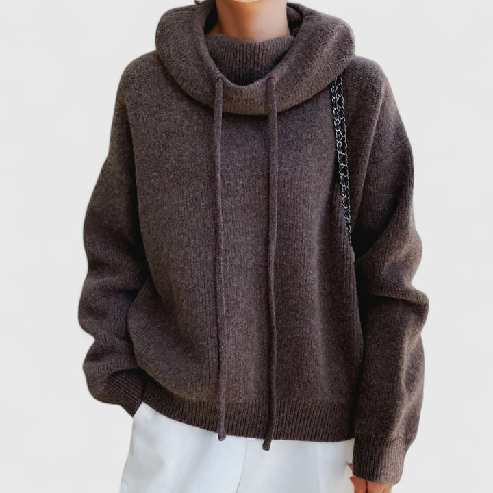 Oversized dark brown knit jumper with a slouchy cowl hood, drawstring detail, and ribbed cuffs against a white background.