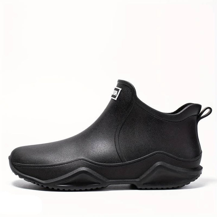 Black waterproof Elodie ankle rain boots with a sleek slip-on design and chunky, grippy wave-tread outsole.
