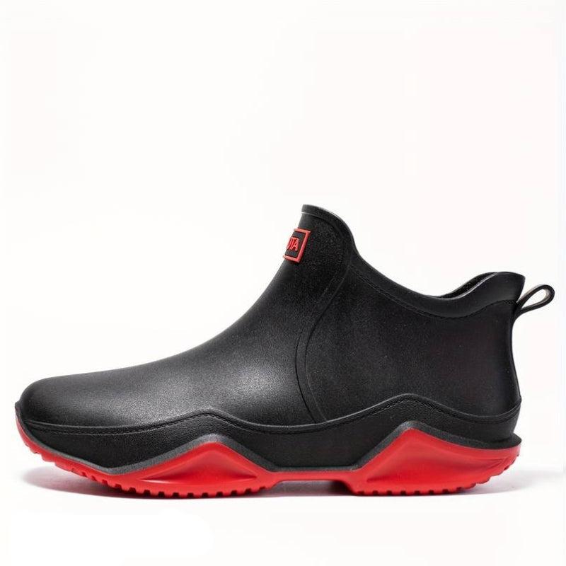 Black waterproof Elodie ankle rain boots featuring a slip-on design and a chunky, high-traction red wave-tread outsole.