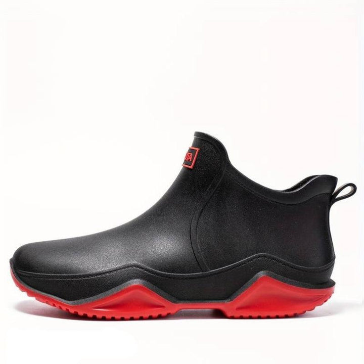 Black waterproof Elodie ankle rain boots featuring a slip-on design and a chunky, high-traction red wave-tread outsole.