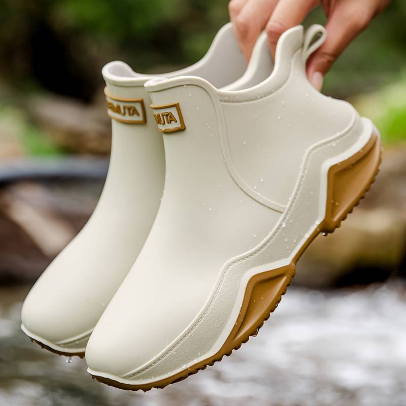 Cream-colored waterproof ankle rain boots with a chunky brown wave-tread sole and convenient slip-on design.