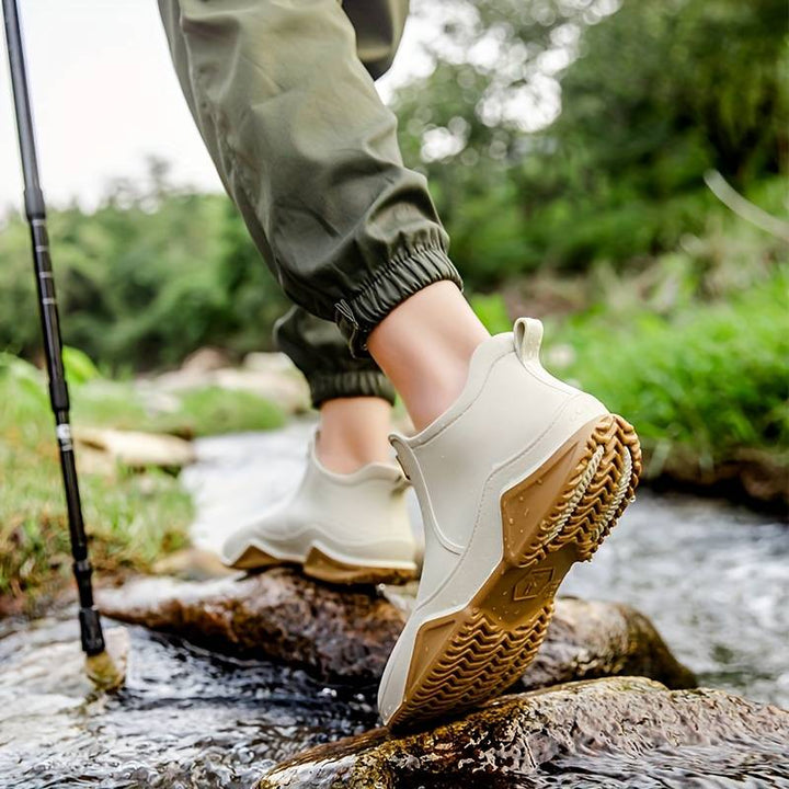 Beige waterproof slip-on ankle rain boots featuring a chunky brown wave-tread outsole for superior grip on wet terrain.